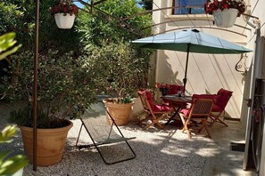 Une terrasse extérieure avec une table et des chaises, entourée de plantes en pot et d’un pot suspendu.