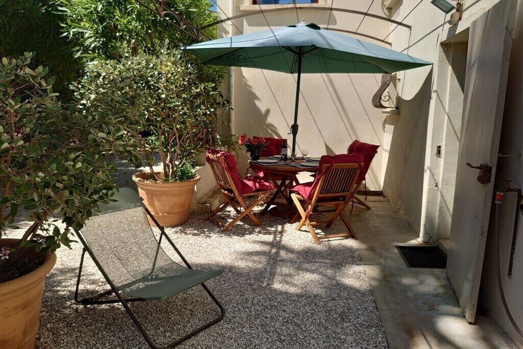 Eine Terrasse im Freien mit Tisch, Stühlen, einem blauen Sonnenschirm und Blumentöpfen.
