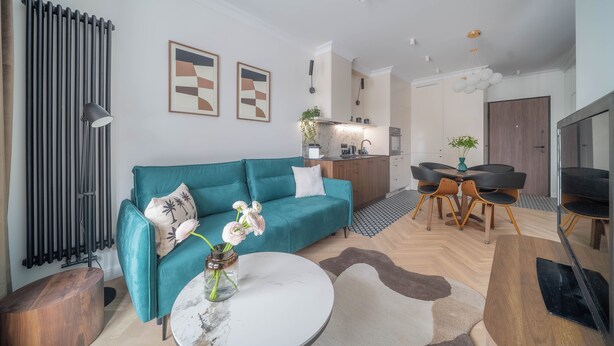 Una sala de estar moderna con un sofá verde azulado, una mesa de centro y un comedor con una mesa y sillas de madera.