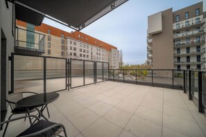 Ein Balkon mit Tisch und Stühlen, Blick auf ein Gebäude mit vielen Fenstern und einem klaren Himmel.