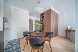 A modern kitchen with a dining area, featuring a round wooden table, black chairs, and a potted plant. - Kierbedzia Elite, Mokotów, Warsaw (Warszawa)