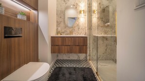 Un baño con inodoro, tocador de madera, salpicadero de mármol y cabina de ducha con mampara de vidrio.