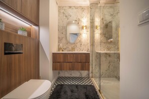 A bathroom with a toilet, wooden vanity, marble backsplash, and a glass shower enclosure. - Kierbedzia Elite, Mokotów, Warsaw (Warszawa)
