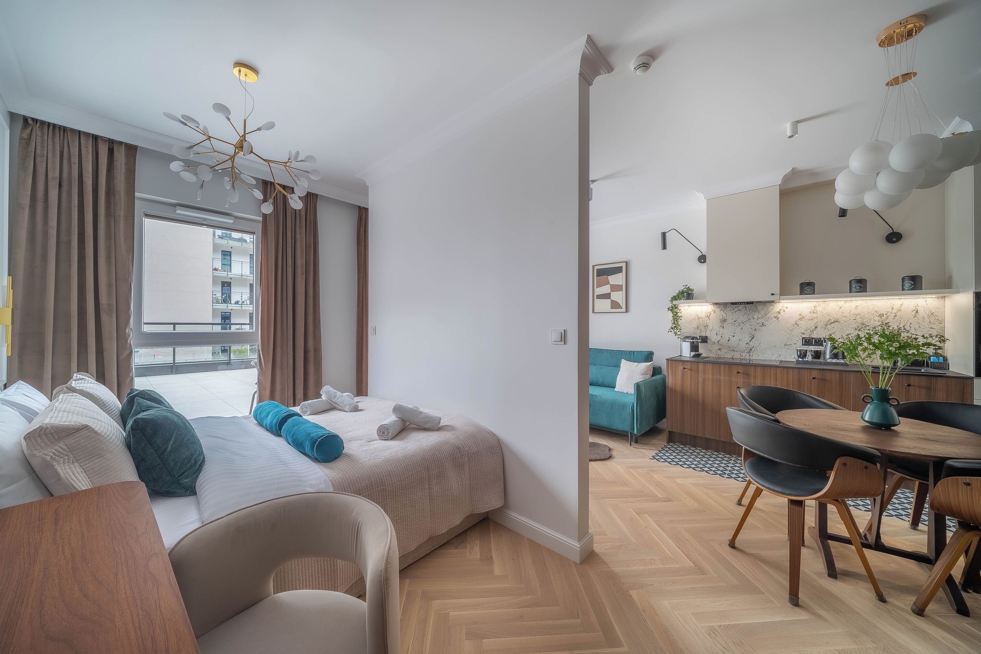 A modern hotel room with a bed, a sofa, a dining area, and a kitchen.