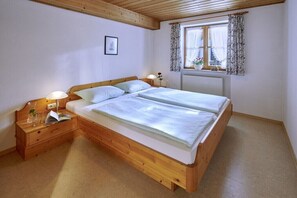 A bedroom with a wooden bed, bedside tables, a window with curtains, and a radiator. - Holiday apartment with 2 bedrooms (Chieming)
