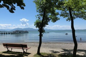 A lakeside view with a bench, trees, and a boat in the distance. - Holiday apartment with 2 bedrooms (Chieming)