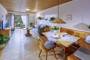 Een ruime woonkamer met een eettafel voor twee personen, een bank en een televisie.