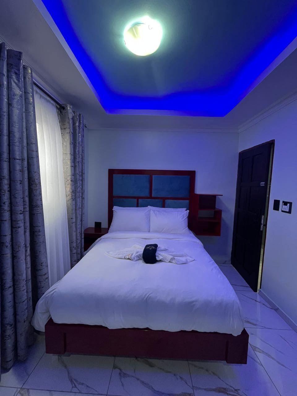 Quarto de hotel com cama, cortinas, mesa de cabeceira e porta.