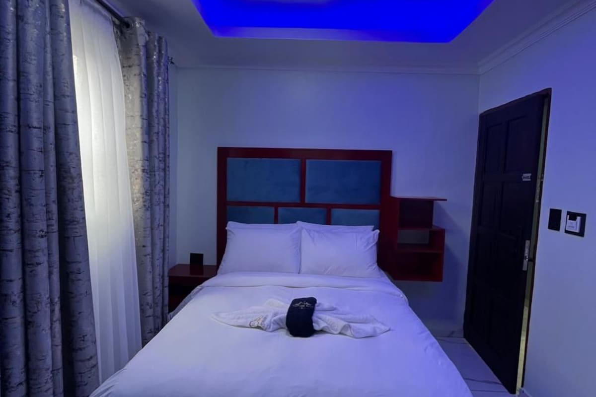 A hotel room with a bed, curtains, a nightstand, and a door.