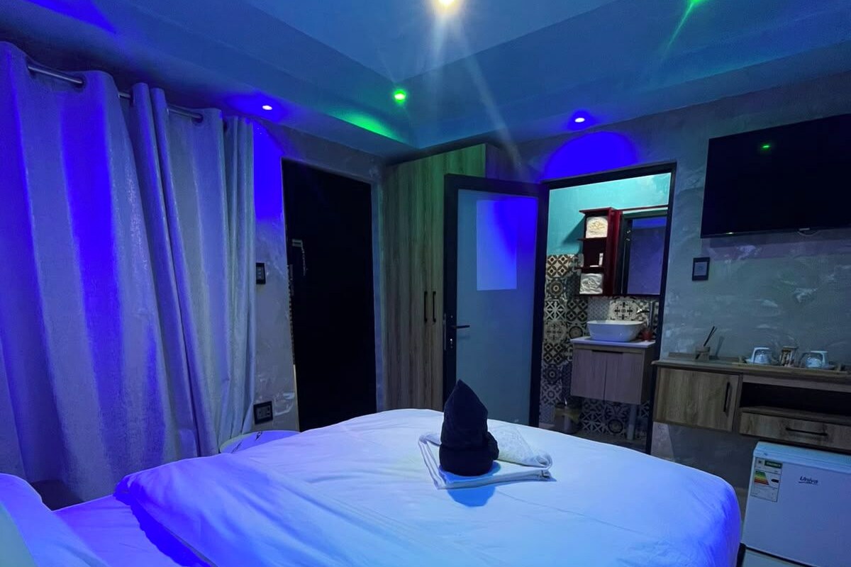 A hotel room with a bed, a flat-screen TV mounted on the wall, and a small kitchenette area.