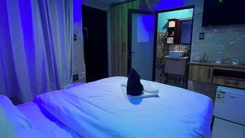 A hotel room with a bed, a flat-screen TV mounted on the wall, and a small kitchenette area.