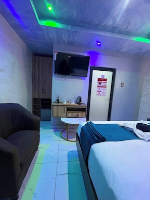 A hotel room with a bed, a sofa, a TV, a small table, and a kitchenette. - Meriambase lodge (Johannesburg)