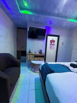 A hotel room with a bed, a sofa, a TV, a small table, and a kitchenette.