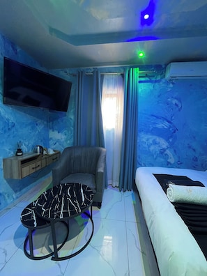 A modern bedroom with a flat-screen TV, a sofa, a round table, and a bed. - Meriambase lodge (Johannesburg)
