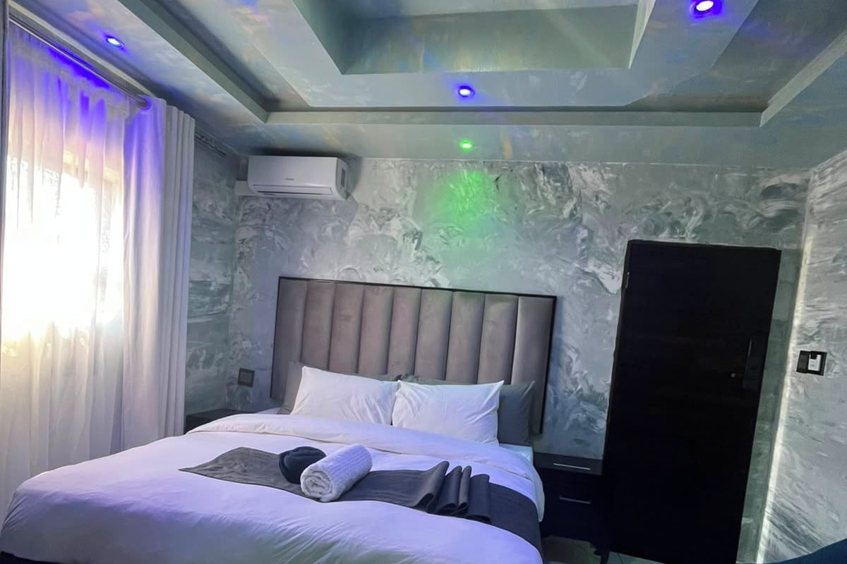A modern bedroom with a bed, nightstands, a wardrobe, and a ceiling with recessed lighting.