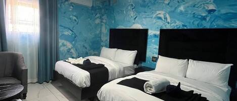 A hotel room with two beds, a chair, and a small table.