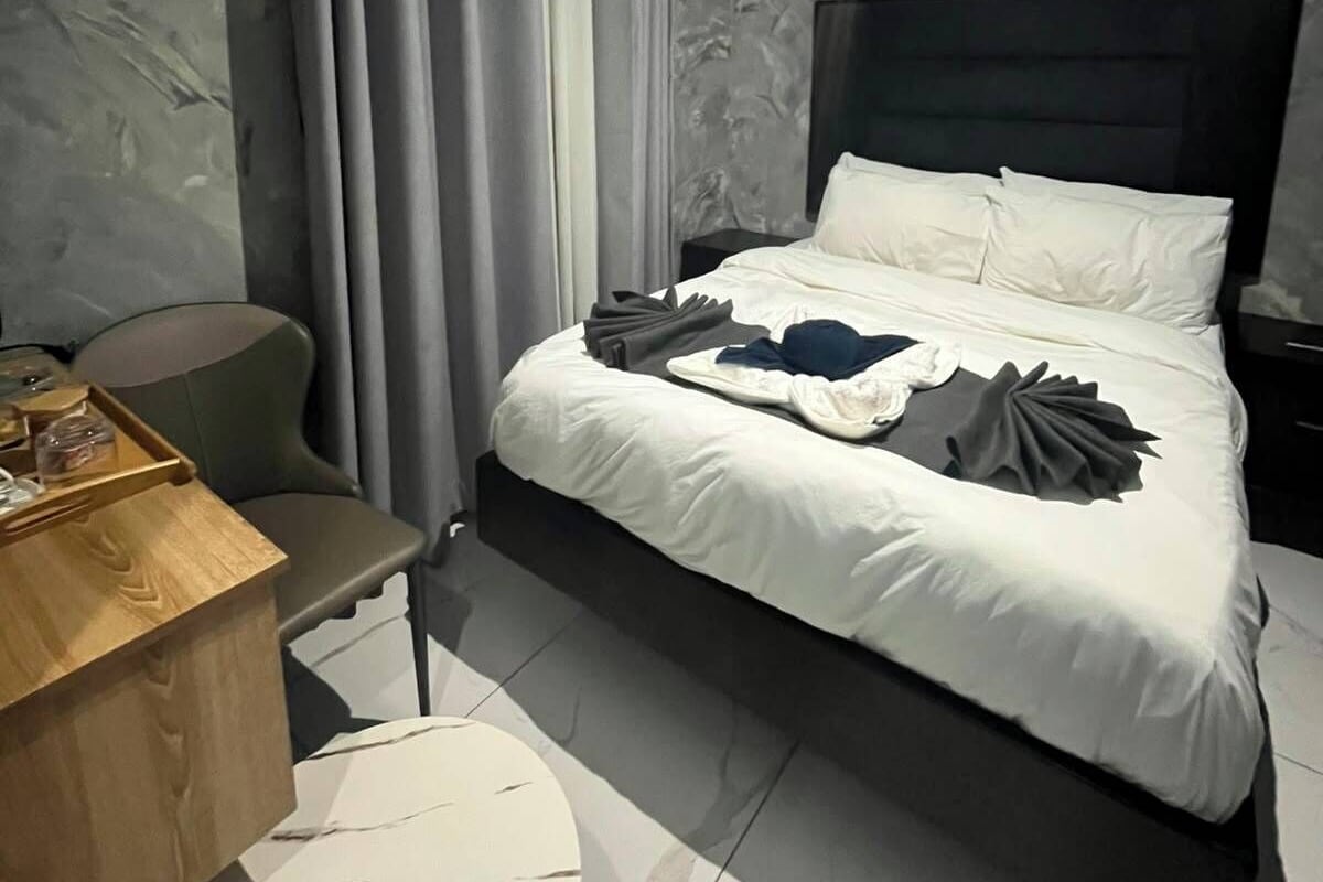 A hotel room with a bed, a desk, a chair, a small table, and a window with curtains.