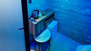 Una habitación pequeña con un televisor de pantalla plana montado en la pared, una mesita con una tetera y una silla.