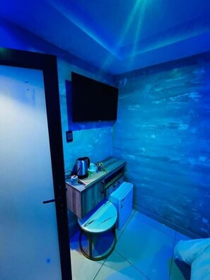 A small room with a flat-screen TV mounted on the wall, a small table with a kettle, and a chair. - Meriambase lodge (Johannesburg)