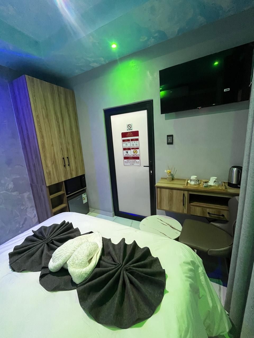 Habitación de hotel con cama, escritorio, televisor y puerta con letrero de seguridad contra incendios.
