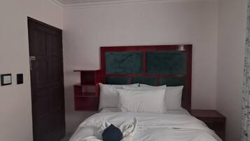 A hotel room with a bed, a nightstand, a red headboard, and a door.