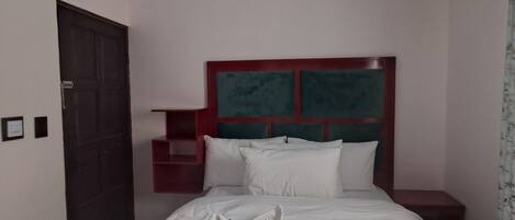 Una habitación de hotel con cama, mesita de noche, cabecera roja y una puerta.