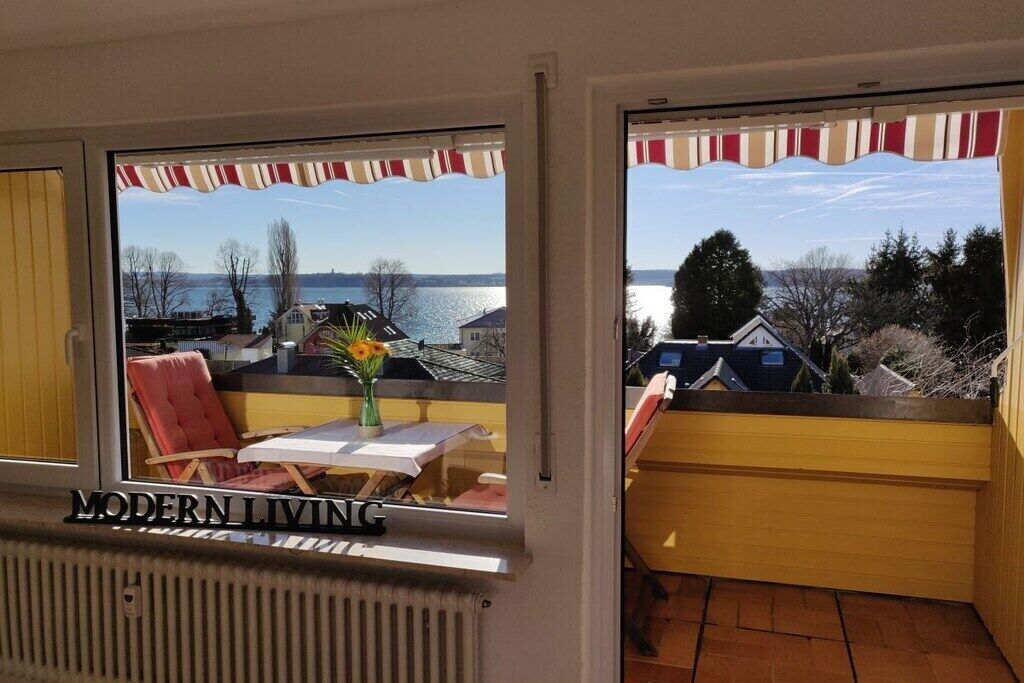 A room with a view of a lake, a table with a vase of flowers, and a chair.