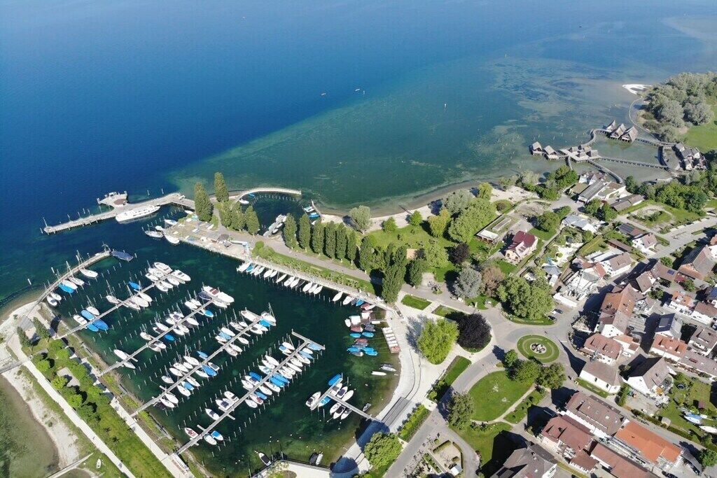 Ovenfra ses en lysthavn med fortøjede både, omgivet af boligbygninger og grøn vegetation.