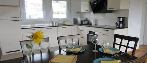 Ett modernt kök med vita skåp, en svart bänkskiva och ett matbord med plats för fyra personer, komplett med blå tallrikar och gula servetter.