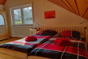 Ein Schlafzimmer mit schrägen Wänden, einem Fenster mit Blick nach draußen, einem Heizkörper und einem Bett mit rot-schwarzem Karomuster.