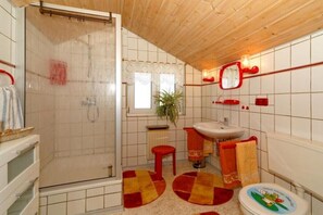 Een badkamer met een douche, wastafel, toilet en een raam.