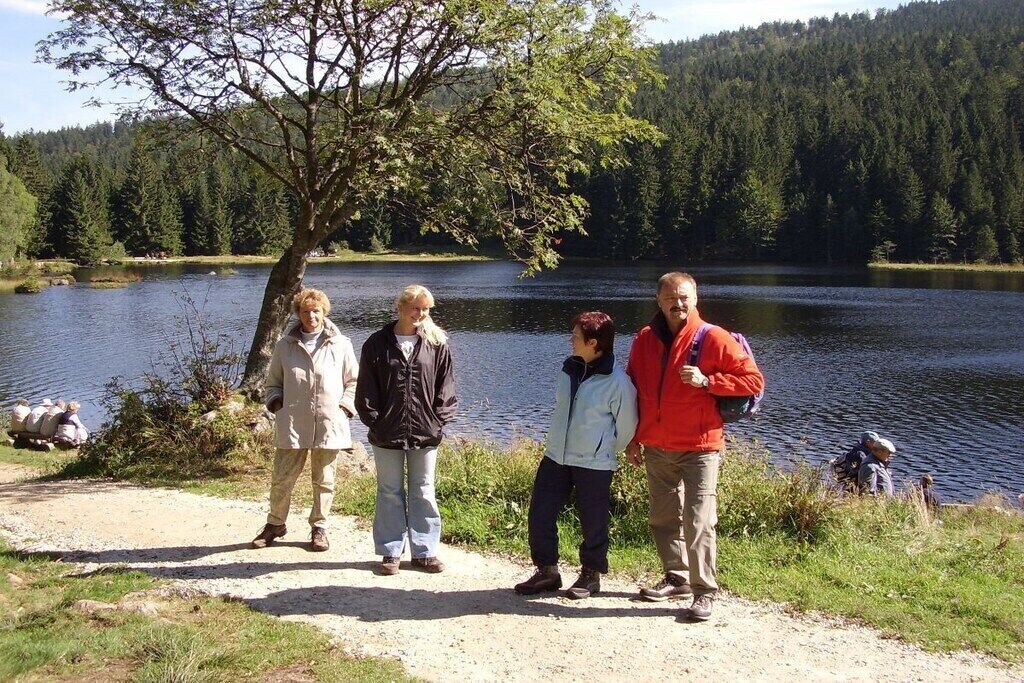 Un grupo de personas de pie junto a un lago con un bosque al fondo.