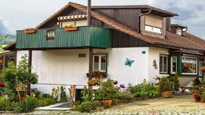 Une maison avec un balcon verdoyant, une décoration en forme de papillon et un jardin où poussent différentes espèces de plantes.