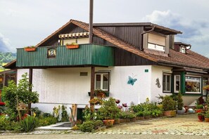 Een huis met een groen balkon, een vlinder decoratie, en een tuin met verschillende planten.