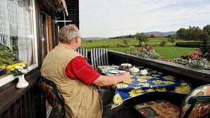 Un homme est assis à une table, face à un paysage verdoyant.