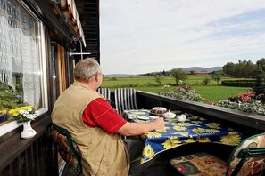 Een man zit aan een tafel met uitzicht op een groen landschap.