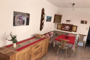 Un comedor con una mesa y sillas de madera, un banco y un camino de mesa rojo.