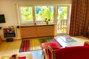 A living room with a large window, a red sofa, a wooden cabinet, and a small table. - Holiday apartment with 2 bedrooms (Reit im Winkl)