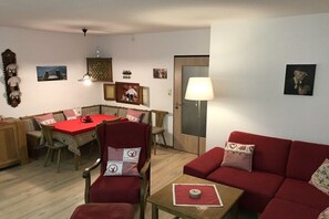 Ein gemütliches Wohnzimmer mit einem roten Sofa, einem Esstisch und einem Tisch mit roter Tischdecke.