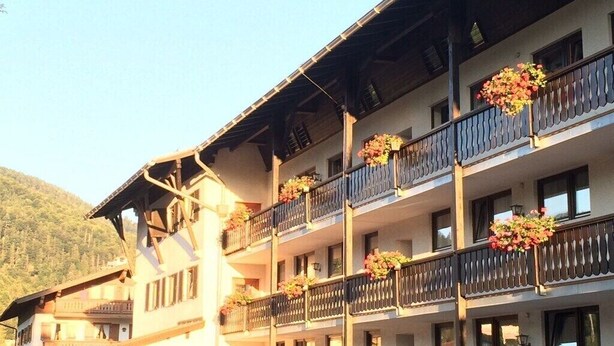 Un hotel de varios pisos con balcones decorados con flores, con montañas al fondo.