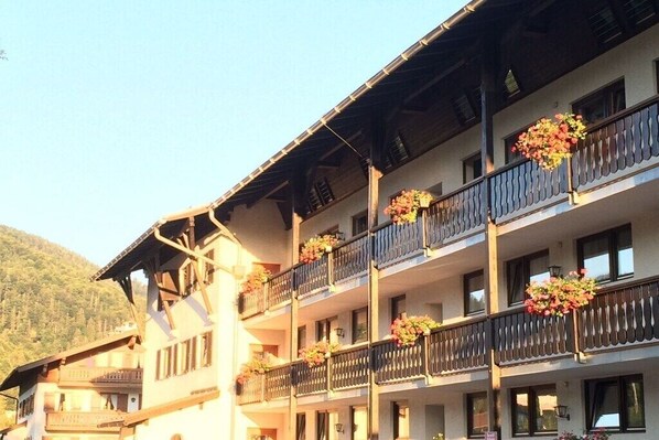 Un hotel de varios pisos con balcones decorados con flores, con montañas al fondo.