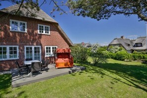 Une maison en briques avec un toit de chaume, une terrasse avec des meubles d’extérieur et une pelouse bien entretenue.