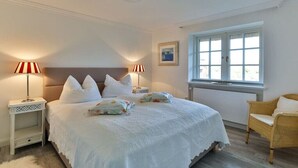 A bedroom with a large bed, two bedside lamps, a window, and a wicker chair. - Holiday home in Kampen with swimming pool (Kampen)