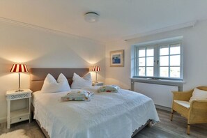 Une chambre avec un grand lit, deux lampes de chevet, une fenêtre et un fauteuil en osier.