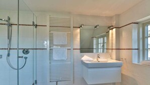 A modern bathroom with a glass shower enclosure, a built-in towel rack, a vanity with a mirror, and a window providing natural light. - Holiday home in Kampen with swimming pool (Kampen)
