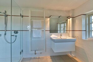 Une salle de bain moderne dotée d’une douche à parois de verre, d’un porte-serviettes intégré, d’un meuble-lavabo avec miroir et d’une fenêtre laissant entrer la lumière naturelle.