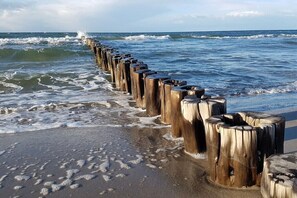 Een houten golfbreker langs een strand, waar golven tegenaan slaan.