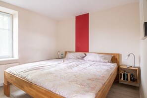 Een slaapkamer met een houten bed, een nachtkastje met een lamp en een boekenkast.