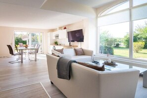 A modern living room with a sofa, coffee table, and a dining area with chairs and a table. - Holiday home semi-detached house Braderup (Dagebüll OT Süderwaygaard)