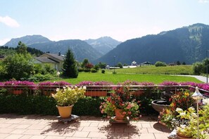 Ein Garten mit Kübelpflanzen und einer Statue, ein gepflasterter Weg und eine Bergkulisse im Hintergrund.